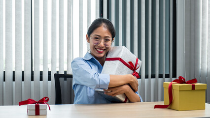 Young asian woman holding big gift box with smiling at office workspace
