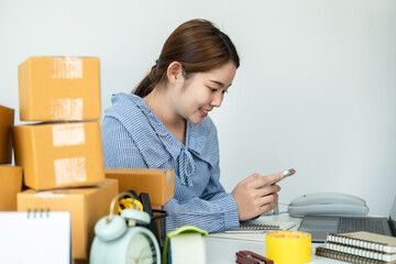 Asian woman small business owner holding smartphone to receive and checking order from customer while working