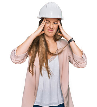 Young blonde woman wearing architect hardhat suffering from headache desperate and stressed because pain and migraine. hands on head.
