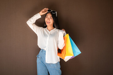 Asian shopaholic woman holding sunglasses headband with many colorful shopping bags