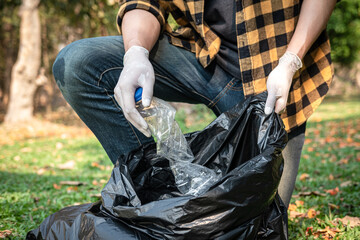 Volunteer man in gloves sitting to squeeze plastic bottles and collect into plastic black bag for cleaning