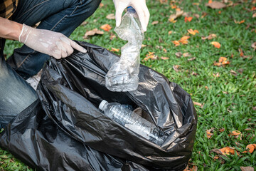 Volunteer man in gloves sitting to squeeze plastic bottles and collect into plastic black bag for cleaning
