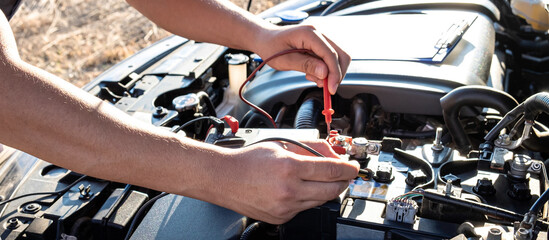 Mechanic checking a car engine with digital voltmeter testing battery capacity, Repair service and...