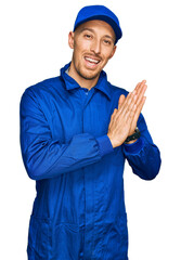 Bald man with beard wearing builder jumpsuit uniform clapping and applauding happy and joyful, smiling proud hands together