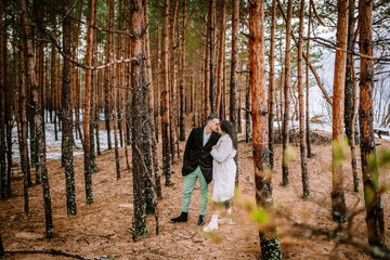 Fototapeta premium couple embracing in a forest. The trees have reddish-brown trunks and there's a sprinkling of snow on the ground