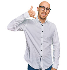 Bald man with beard wearing business shirt and glasses smiling doing phone gesture with hand and fingers like talking on the telephone. communicating concepts.
