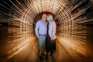  happy couple standing close together, surrounded by a mesmerizing tunnel of golden light streaks...