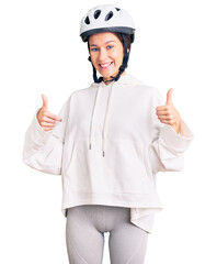Beautiful brunette young woman wearing bike helmet and sporty clothes success sign doing positive gesture with hand, thumbs up smiling and happy. cheerful expression and winner gesture.