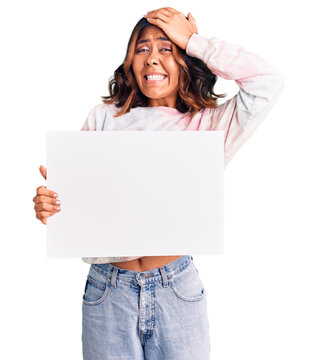 Young beautiful mixed race woman holding cardboard banner with blank space stressed and frustrated with hand on head, surprised and angry face