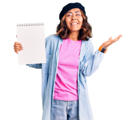 Young beautiful mixed race woman wearing artist look with beret holding notebook celebrating victory with happy smile and winner expression with raised hands