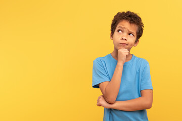 Pensive boy contemplating, looking aside at copy space on yellow background