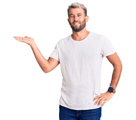 Young handsome blond man wearing casual t-shirt smiling and looking at the camera pointing with two hands and fingers to the side.