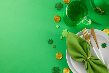Preparing the table for St. Patrick's Day gathering. Top view shot of plates, cutlery, green napkin, leprechaun hat, pint of green beer, gold coins, clovers on green background with well-wishing space