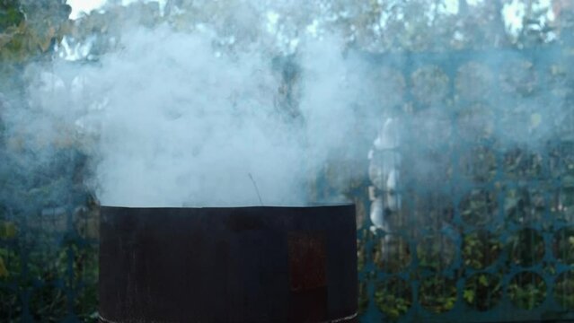 Garden and house garbage burning in a bin incinerator close up. A cat climbs a fence in the background
