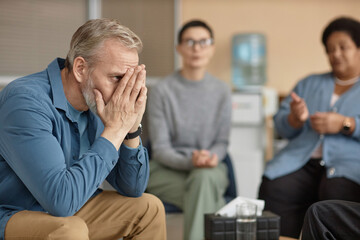 Side view portrait of depressed senior man crying in group therapy session and hiding face, copy...