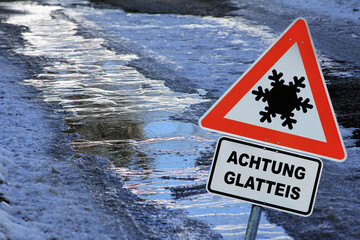 Schild mit Achtung Glatteis auf einer vereisten Straße