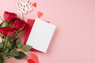 The delightful mood of Valentine's festivities. Top view shot of red envelope with card, red roses, paper hearts on pastel pink background with greetig space