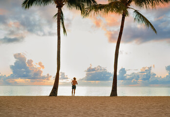 ..Running teenage boy between tall palm trees on Flic en Flac beach with incredible sunset time...