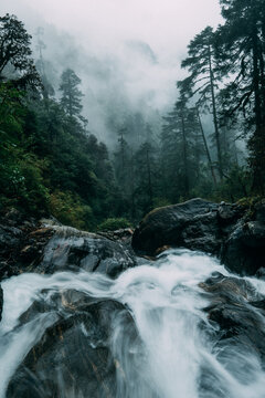 Powerful mountain creek running through the big boulders down the foggy rain forest jungles in Makalu Barun National Park near Chatra Khola settlement. Mera peak climbing route, Himalayas, Nepal.