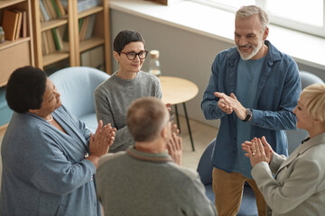 High angle view at group of senior people standing in circle and applauding celebrating success in support meeting