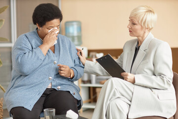 Fototapeta premium Portrait of depressed Black senior woman crying in therapy session with caring female psychologist
