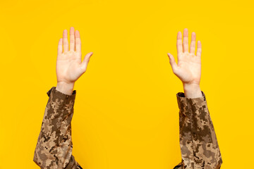 I give up. empty hands of a ukrainian military man raised up on a yellow isolated background, a...