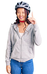 Young beautiful chinese girl wearing bike helmet pointing finger up with successful idea. exited and happy. number one.