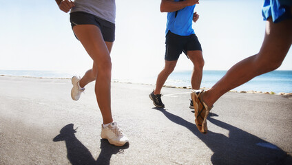 People, fitness and legs running at beach for exercise or outdoor workout together on asphalt or...