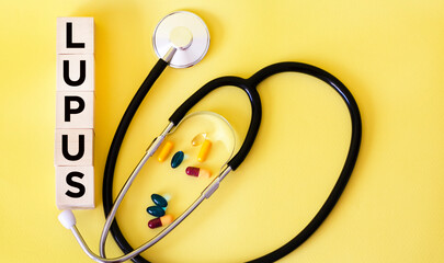 The word Lupus is written on wooden blocks and a stethoscope on a yellow background. Conceptual healthcare for hospitals, clinics and medical business.
