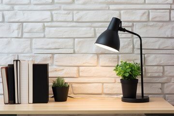 Modern wooden table with desk lamp and books on brick wall background