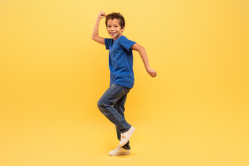 Fototapeta na wymiar Joyful boy dancing in blue shirt on yellow background