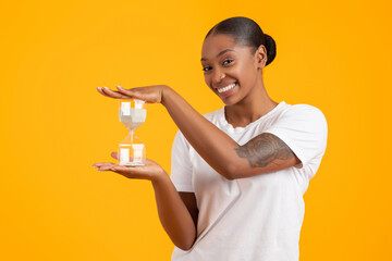 Cheerful African American Woman Holding Sand Clock Over Yellow Background