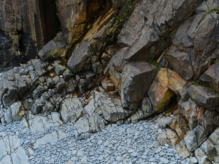 Wave action and weather smoothed gray rocks at the foot of steep rocky cliffs on the Newfoundland coast