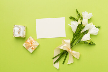 White freesia flower and gift box with diamond ring on color background, top view