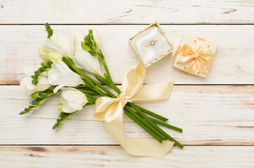 White freesia flower and gift box with diamond ring on wooden background, top view