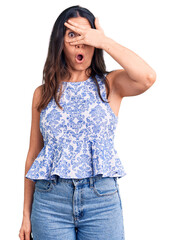 Young beautiful brunette woman wearing casual t-shirt peeking in shock covering face and eyes with hand, looking through fingers with embarrassed expression.