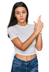 Young hispanic girl wearing casual white t shirt holding symbolic gun with hand gesture, playing killing shooting weapons, angry face