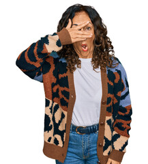 Middle age hispanic woman wearing casual clothes peeking in shock covering face and eyes with hand, looking through fingers with embarrassed expression.