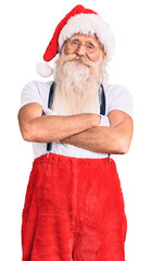 Old senior man with grey hair and long beard wearing santa claus costume with suspenders happy face smiling with crossed arms looking at the camera. positive person.