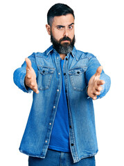 Hispanic man with beard with open arms doing hug gesture skeptic and nervous, frowning upset because of problem. negative person.