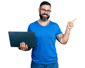 Hispanic man with beard working using computer laptop smiling happy pointing with hand and finger to the side