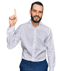 Naklejka premium Young man with beard wearing business shirt showing and pointing up with finger number one while smiling confident and happy.