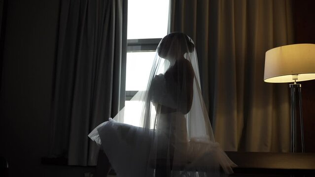 A beautiful bride touches herself tenderly while covered with a veil 