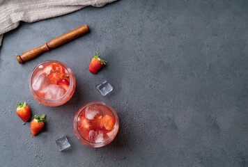 Brazilian strawberry caipirinha in glasses with ice and fruits over stone background with copy space