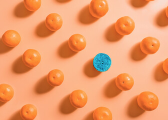 A vibrant image of a pattern of fresh tangerines on a soft peach background with one blue tangerine in the group, can be used to convey the concepts of unity, similarity and difference