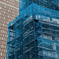 building under construction covered in blue mesh tarp protective wrap (safety debris netting during...