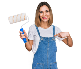 Young blonde girl holding roller painter pointing finger to one self smiling happy and proud