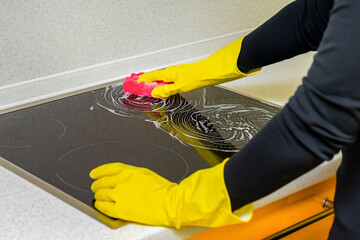 woman in rubber gloves washes the hob in the kitchen.