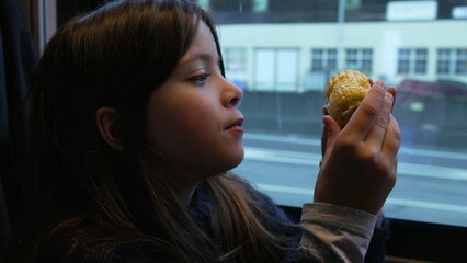 One small girl eating corn while inside a moving train. Child snacking healthy food while scenery passes by in background