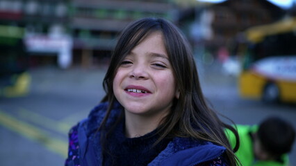 Portrait of a happy small girl chuckling at camera standing in urban setting. Closeup face of child wearing blue jacket